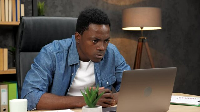 Shocked African American businessman looks at laptop screen display worried of problem in office. Frustrated adult man student read bad online news receive failed exam results, sits on chair at table