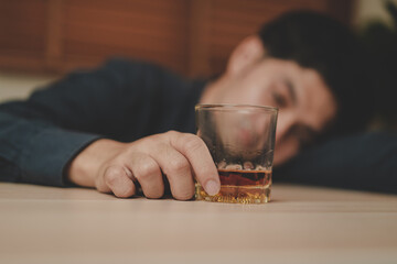 Alcoholism, depressed asian young man sleep on table while drinking alcoholic beverage, holding glass of whiskey alone at night. Treatment of alcohol addiction, suffer abuse problem alcoholism concept