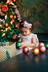 Fototapeta na wymiar a little African-American girl in a pink dress is playing with Christmas balls to decorate the Christmas tree. a child decorates a fir tree with colorful balls