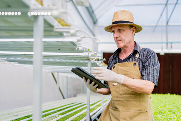 Caucasian male business owner observes about growing organic arugula on hydroponics farm.with tablet on aquaponic farm, sustainable business artificial lighting,Concept of growing organic vegetable