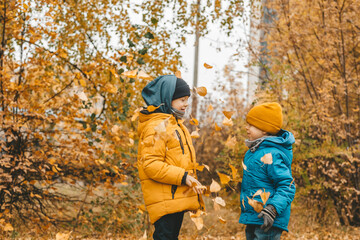 Naklejka premium boys in a jacket scatter leaves in an autumn park. The child rejoices in the autumn leaves. The boys are happy about autumn. Walking in the autumn park. Happy childhood
