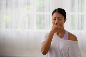 To guide her breath, an Asian lady touches her nostrils with her fingers. To get started with yoga and meditation