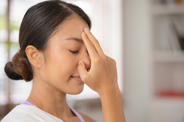 To guide her breath, an Asian lady touches her forehead with her fingers. To get started with yoga and meditation