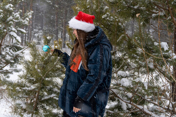 young woman in santa hat with christmas ball in winter in forest