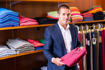 Young elegant man visiting clothing store in search of new look, choosing stylish polo shirt