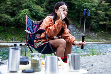川辺でキャンプをする女性／スマートフォンで撮影をしている