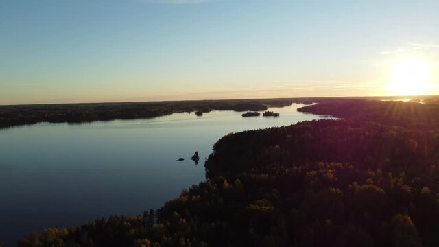 Cinematic drone shot of tranquil River surrounded by wild forest landscape during sunset lights and blue sky - Finland,Northern Europe