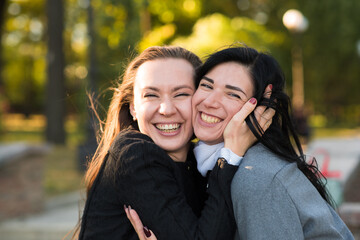 Fototapeta premium Two Caucasian brunette girls are hugging in the sunny autumn park. Happy lesbian couple, lgbt, lgbtq.
