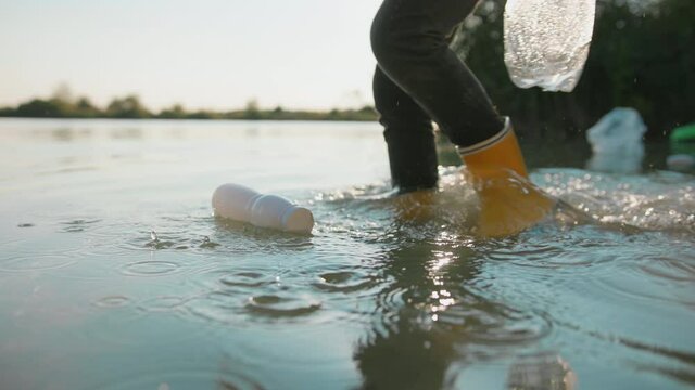 Closeup young boy walking in polluted river water and collecting garbage waste plastic bottle leftovers. Cleaning pond. Ecology. Save environment.