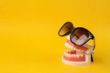 Minimal summer concept. Plastic model of a human jaw with sunglasses on yellow background