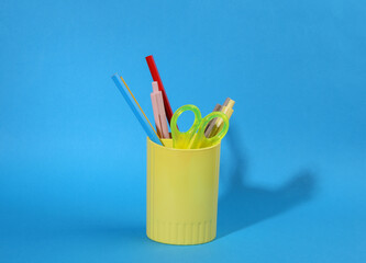 Colored pencils and various colorful stationery for school in holder or cup on blue background