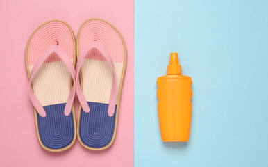 Colored flip flops with sunblock bottle on blue-pink pastel background. Beach vacation concept. Flat lay