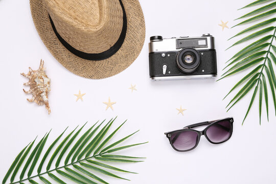 Travel flat lay. Hat with sungglasses, starfish, seashells and camera, palm leaves on white background. Top view