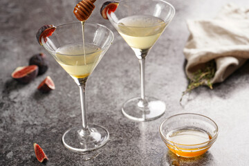 Two martini glasses with alcoholic beverage liquor with thyme branch, honey and figs on grey marble surface