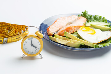 Plate with food, alarm clock and measuring tape on white background.