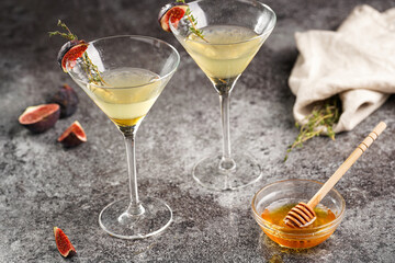 Two martini glasses with alcoholic beverage liquor with thyme branch, honey and figs on grey marble surface