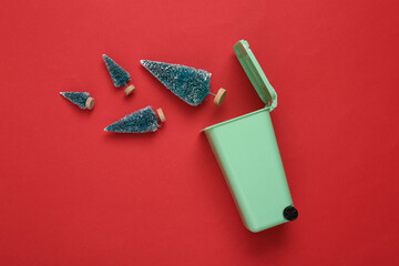 Miniature trash can with Christmas trees on red background. Christmas recycling garbage concept