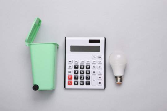 Toy trash can with led light bulb and calculator on gray background. Recycling, eco concept. Top view, flat lay