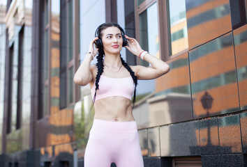 Portrait of a cute fit brunette woman with pigtails and in headphones on the background of a city building