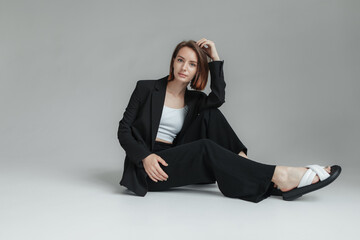 Fashion shot of stylish vogue woman in black suit sitting on floor in studio