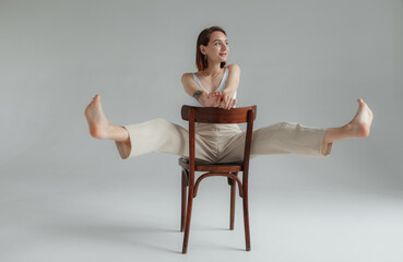 Young barefoot loosened woman sits on a wooden chair in gray studio. Lifestyle. Fashion snapshot