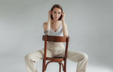 Young stylish woman sitting on wooden chair on gray background