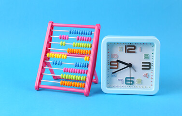 Colored abacus and alarm clock on blue background. Counting, education, economy, business and...