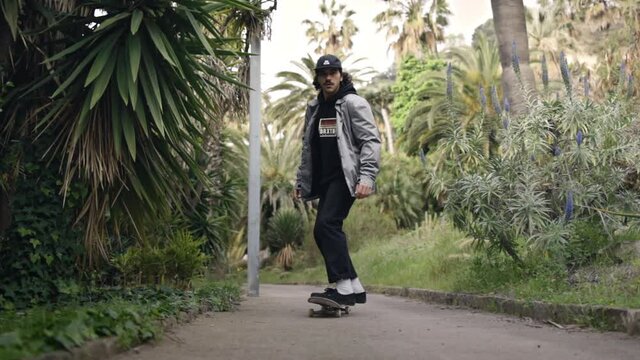 Young Skater skating in garden walkway with palmtrees, tracking shot