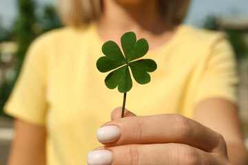 Woman holding green four leaf clover outdoors, closeup - Powered by Adobe