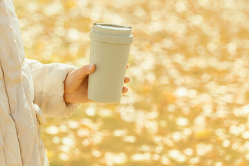 Man holds in her hand  bamboo cup with lid on autumn blurred background with bokeh, zero waste concept