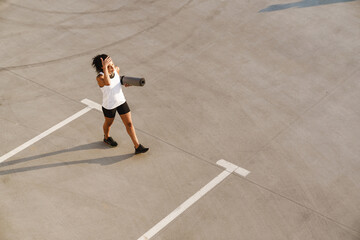 Black sportswoman working out with fitness mat on parking