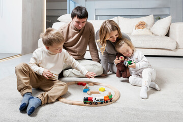Happy young family with small children are sitting and playing on the floor in a bright living room. Love, tenderness and warm relationships.
