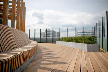 Panorama view of modern rooftop terrace with dark wood deck flooring, plants, brick fence and black garden furniture