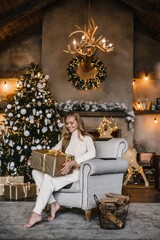 Fototapeta na wymiar young beautiful woman model with long hair in a beige suit christmas tree christmas In brown wooden houses 