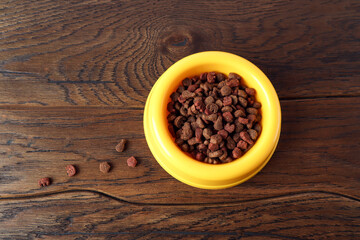  Cat granulated food in a yellow bowl on a wooden surface, top view , close-up, place for text