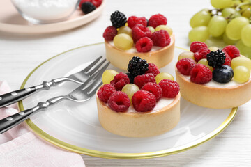 Delicious tartlets with berries on white wooden table