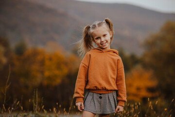 Girl in orange hoodie and skirt posing against autumn mountains