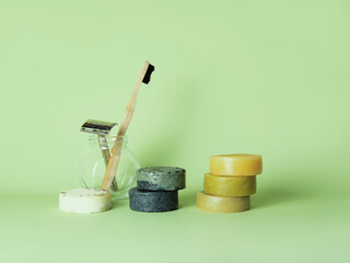 The bamboo toothbrush and the steel multiple-use razor in the glass and six natural round soaps for different uses against the green background. Zero waste bathing concept.