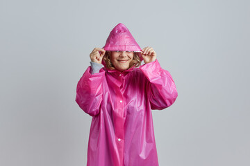 Senior happy woman in magenta raincoat hides her face from the rain under the hood