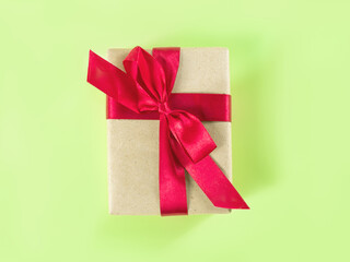 The above view on the packed present in the craft paper with the red satin ribbon on the light green background.
