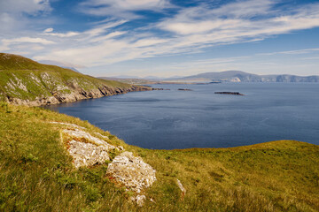 Fototapeta na wymiar View on amazing Keem bay from a top of a mountain. Warm sunny day. White clouds on blue sky. Spectacular Irish nature landscape. Achill island, Ireland. Nobody. Cliffs and coast line.