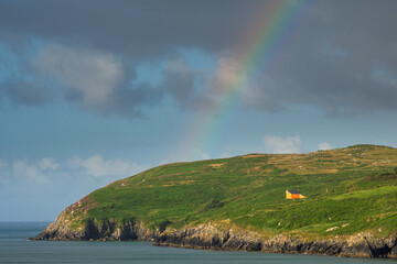View on Mizen Peninsula in county Cork, Ireland. Colorful rainbow symbol of luck in the sky. Calm water of Atlantic ocean and green fields. Irish landscape. Popular travel destination. Nature wonder. - obrazy, fototapety, plakaty