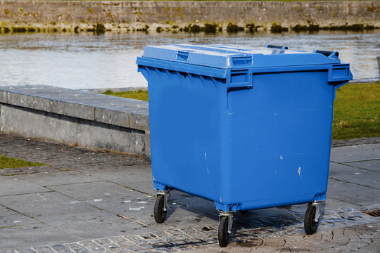 Blue big size wheelie bin in town by a river. Waste and recycle management industry.
