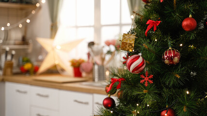 kitchen at Christmas time in bright modern home interior. focus view on xmas tree in side with blurred back view of cooking place in apartment. red and gold balls decorations hanging on tree