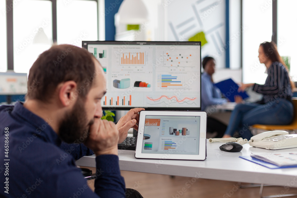 Poster businessman in wheelchair analyzing digital financial graph using tablet computer working at managem