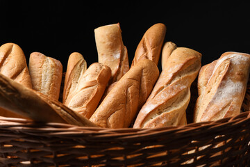 Fresh tasty baguettes in basket against black background, closeup