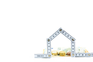 Folded folding rule in the shape of a house, behind it bills and coins