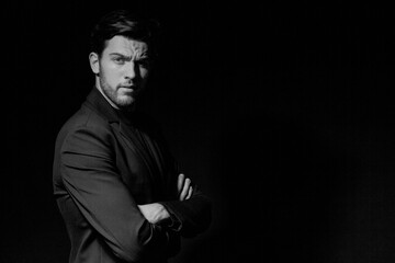 Fototapeta na wymiar Portrait of Handsome Caucasian Brunet Businessman Wearing Black Suit Posing With Hands folded Against Black Studio Background