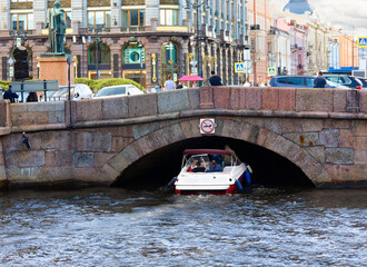 A motorboat sails under a bridge, under a sign prohibiting passage for small vessels. Danger to passengers. The river channel. Photo.