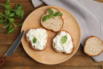 Bread with cottage cheese and basil on wooden table, flat lay